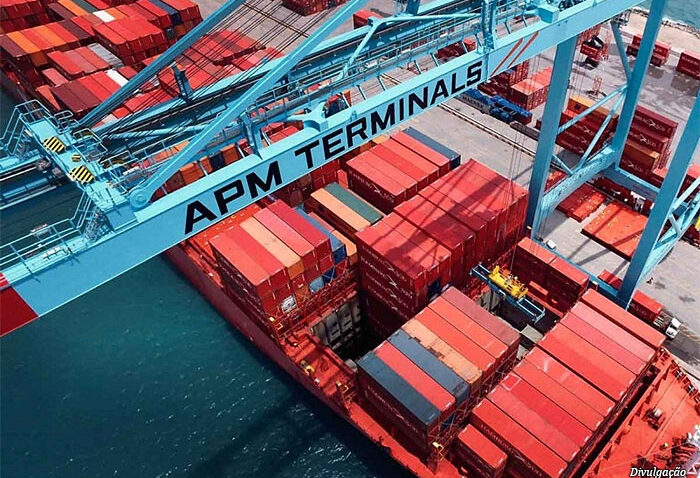 Vista aérea de um navio cargueiro no porto, com contêineres em pilhas vermelhas e a estrutura do casco exibindo a inscrição “APM TERMINALS”.