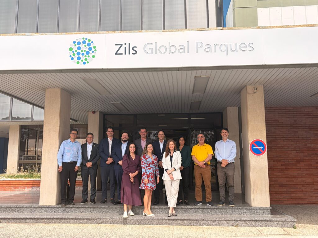 Foto de um grupo de pessoas posando em frente à fachada do Zils Global Parques, em um prédio com entrada ampla e letras de identificação na parede.