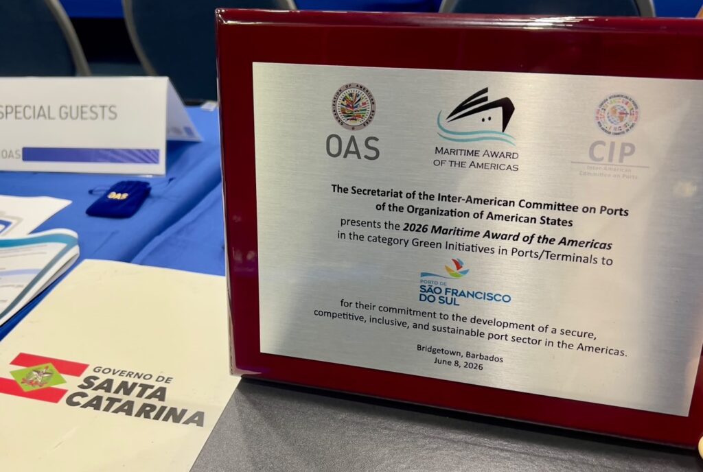 Placa de premiação com o texto “Maritime Award of the Americas” e “OAS”, na cor vermelha, ao lado de materiais com o destaque “Governo de Santa Catarina”.
