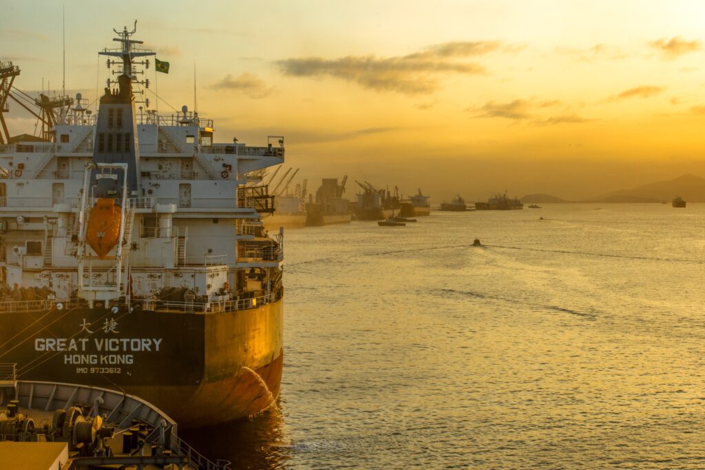Navio cargueiro atracado no cais ao pôr do sol, com céu dourado e vários outros barcos ao fundo em uma viagem no mar.