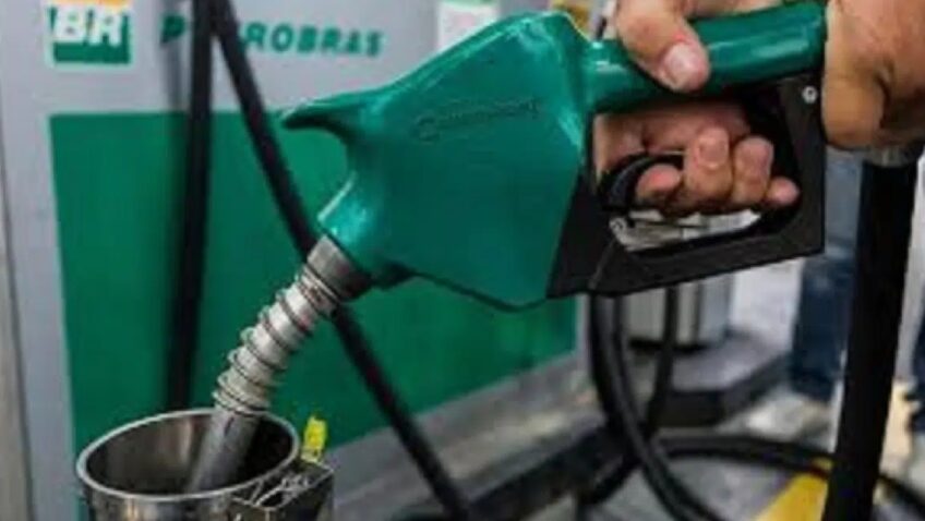 Pessoa abastecendo um carro em posto de combustível, segurando a pistola verde e inserindo o bico no tanque. Cena de abastecimento na bomba de gasolina.
