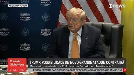 Donald Trump em conferência à frente de um fundo com bandeira dos Estados Unidos, em coletiva de imprensa, ao lado de texto de noticiário na tela.