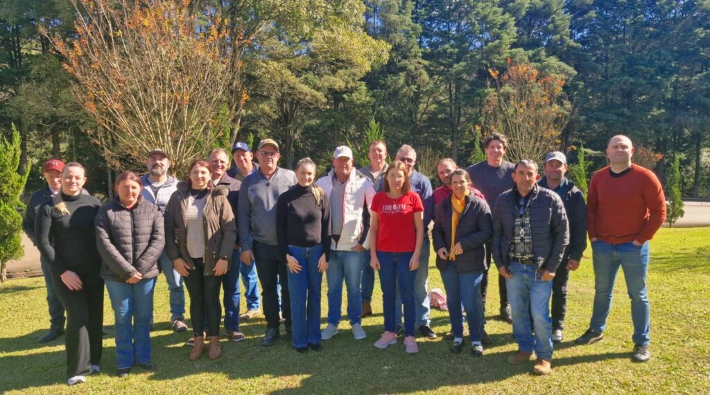 Grupo de pessoas posando para foto em um jardim, ao ar livre, com gramado e árvores ao fundo em um dia ensolarado.