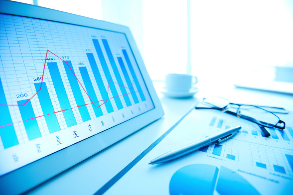 Gráfico de barras e linhas em uma tela de monitor com dados de análise, ao lado de calculadora e caneta sobre uma mesa, representando planejamento e indicadores financeiros.