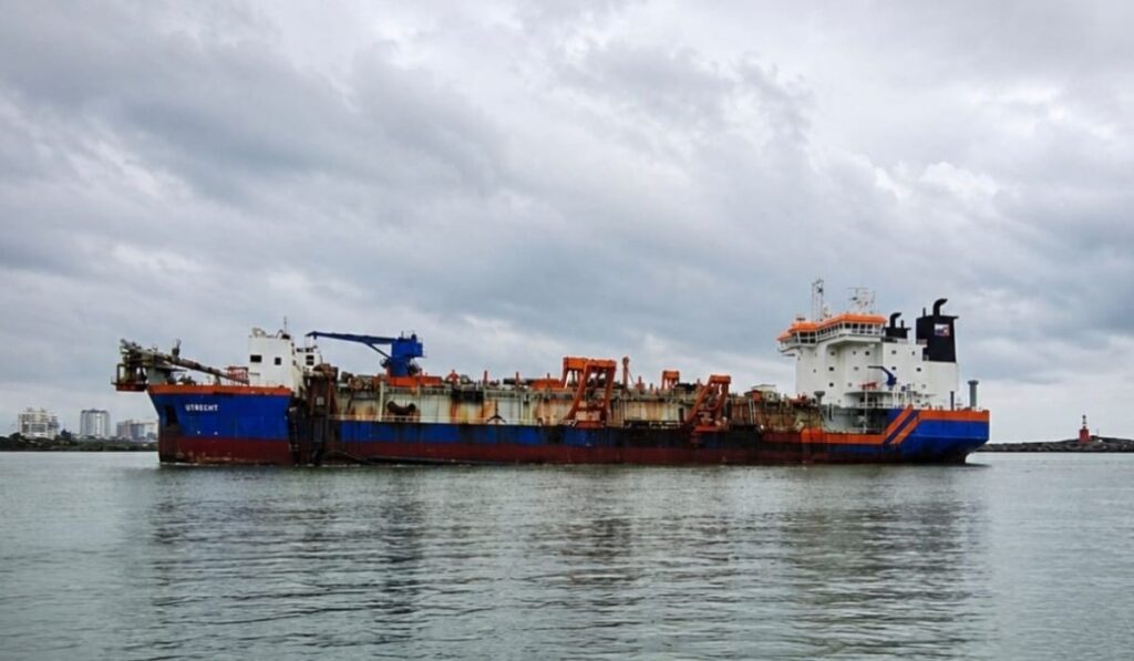 Navio de carga tipo graneleiro no porto, em vista lateral, com guindastes e equipamentos de movimentação no convés, atracado sobre as águas.