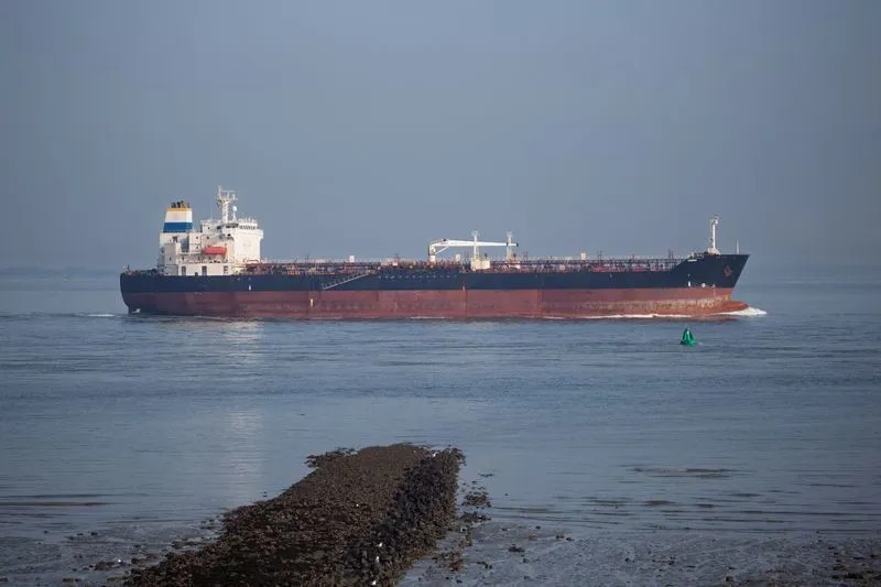 Navio petroleiro de grande porte navegando no mar ao fundo em uma cena com água calma e iluminação crepuscular, com casco vermelho e estrutura branca ao longo do convés.