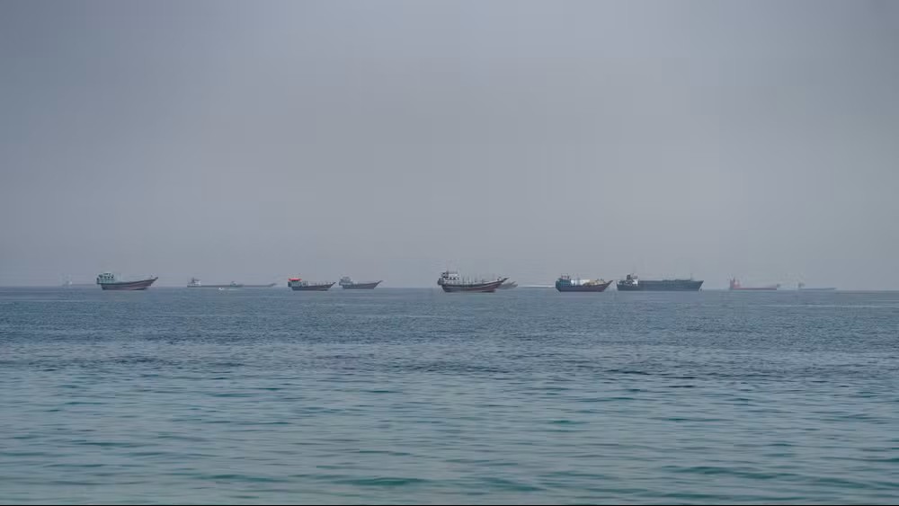 Barcos cargueiros navegando ao longe no mar em um dia nublado, vistos a partir da água com leve neblina no horizonte e várias embarcações na mesma rota.