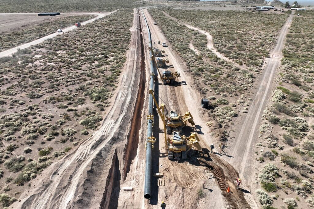 Vista aérea de obras de construção de uma rodovia em área rural, com máquinas pesadas e caminhões trabalhando ao longo do canteiro central de uma estrada recém-formada em meio a vegetação seca.