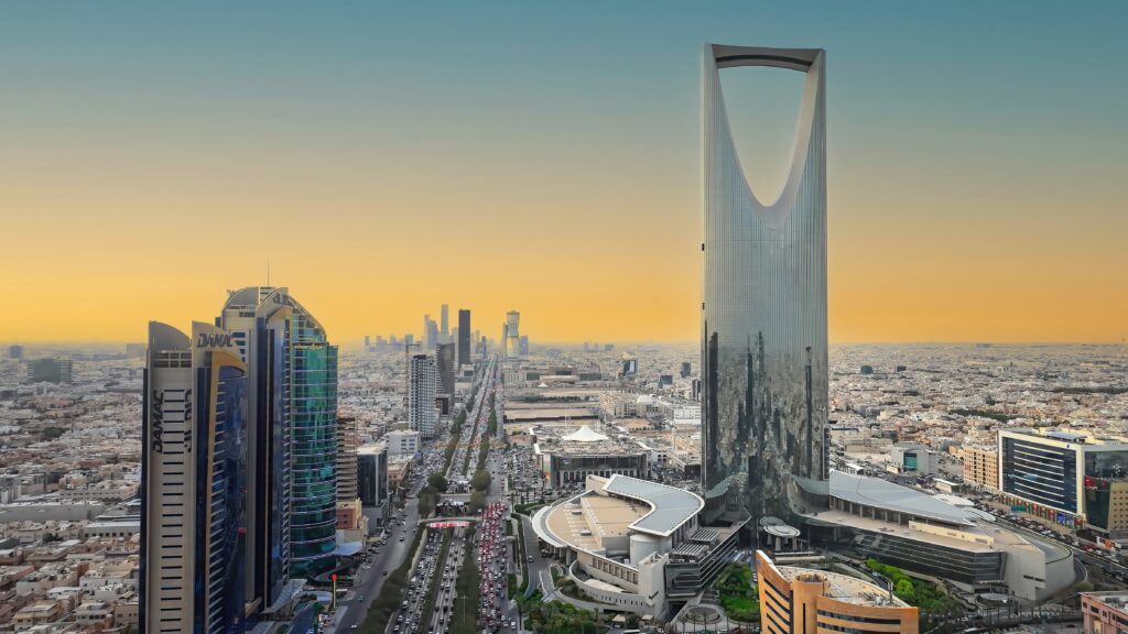 Vista panorâmica de um skyline urbano ao entardecer, com arranha-céus e um grande edifício central envidraçado, ruas movimentadas e horizonte de cidade