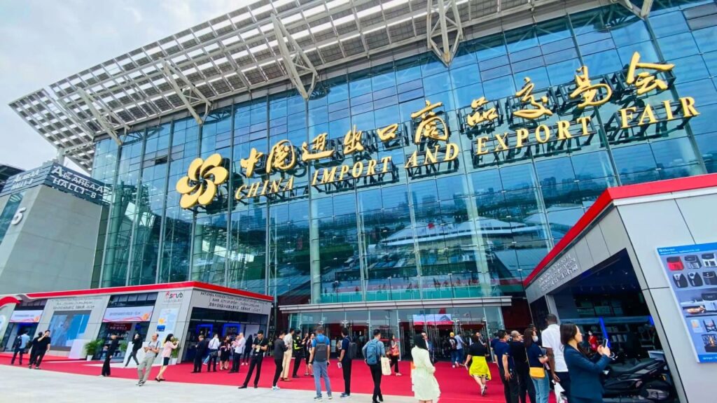 Fachada de um pavilhão em feira internacional com letreiro “China Import and Export Fair” e pessoas circulando na entrada, ambiente de evento corporativo