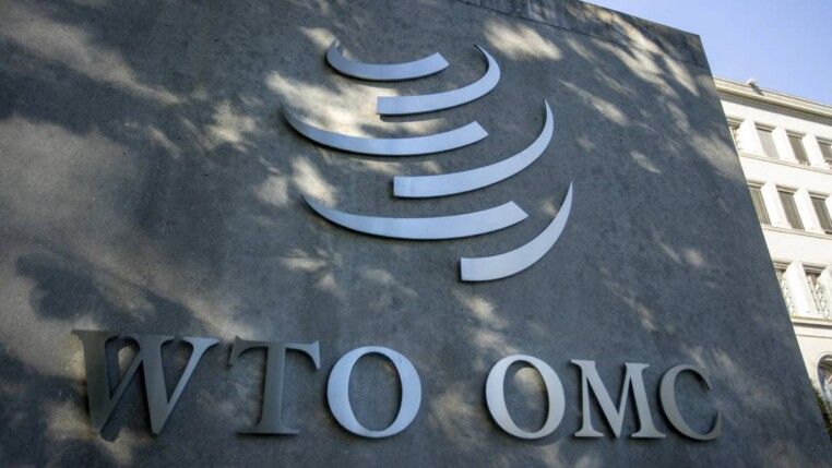 Placa de fachada do banco WIO OMC com letras metálicas e símbolo em relevo sobre superfície escura, vista externa ao ar livre.