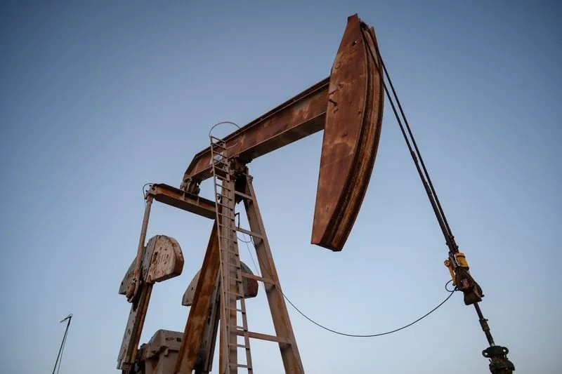 Bomba de extração de petróleo em operação, com grande estrutura metálica enferrujada e haste do poço ao céu claro