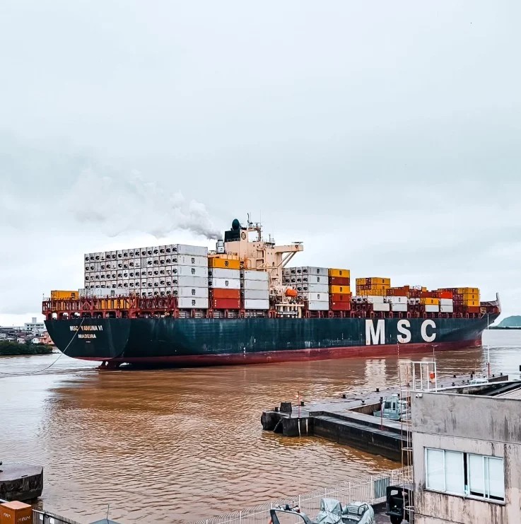 Navio cargueiro da MSC carregado de contêineres atracado no porto, com vista da água e da estrutura de doca ao lado.